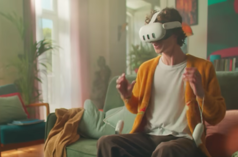 Mann sitzt mit weißer Meta Quest 3 auf dem Sofa und gestikuliert mit den händen